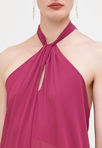 Robe dos nu en tissu transparent de magenta profond, avec un lien torsadé au cou et un détail en trou de serrure. Texture lisse, design minimaliste.