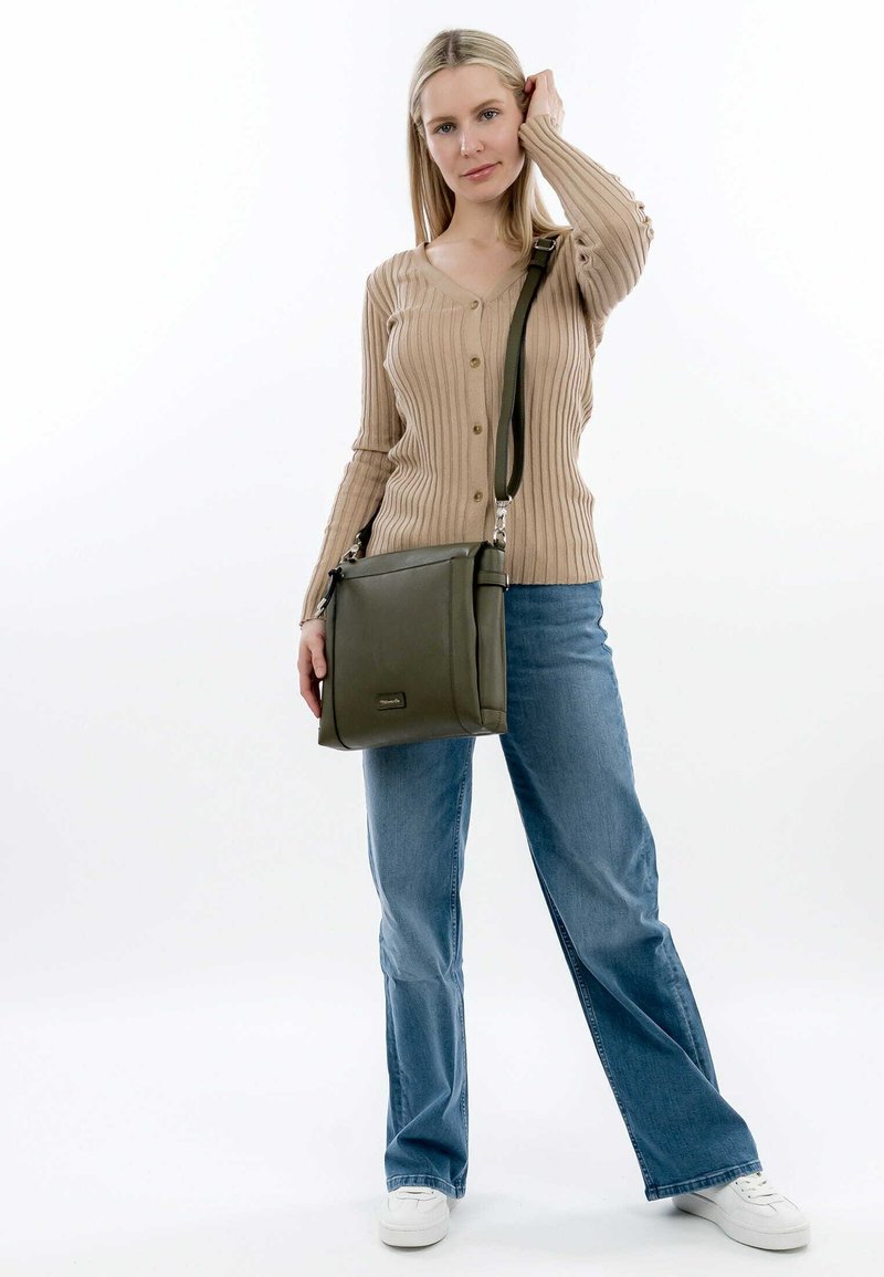 Borsa a spalla in pelle verde oliva con design piatto e parti metalliche argentate, indossata con una tracolla regolabile. Cardigan beige a coste e jeans blu.