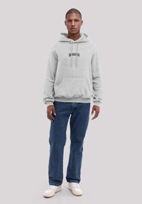 Gray hoodie with front pocket and drawstrings, featuring "BROOKLYN" printed in black. Paired with blue denim jeans and white sneakers.