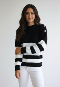 Czarnobiały sweter w paski o prążkowanej fakturze, z okrągłym dekoltem i ozdobnymi guzikami na ramieniu.