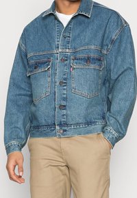 Jeansjacka i mellangunblå färg med knappar framtill, två bröstfickor och en avslappnad passform. Texturerat tyg med kontrasterande sömmar.