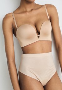 Beige lingeriesetje met een gevormde beha met een diepe halslijn en hoge slips. Glad materiaal met een naadloos ontwerp.