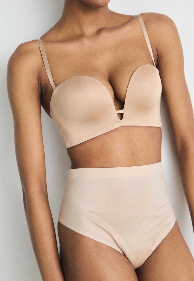 Beige lingeriesetje met een gevormde beha met een diepe halslijn en hoge slips. Glad materiaal met een naadloos ontwerp.