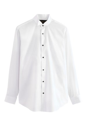 Chemise blanche à manches longues avec boutons noirs, col pointu et poignets boutonnés, présentée sur un fond uni.