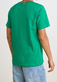 Green cotton t-shirt with a crew neck and short sleeves, featuring a plain design. Worn with light blue denim shorts.