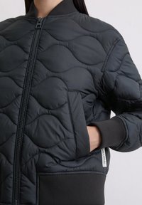 Czarna pikowana kurtka bomberka z fakturowanym wzorem, ściągaczami na mankietach i bocznymi kieszeniami. Posiada frontowy zamek błyskawiczny oraz metkę z logo na dole.