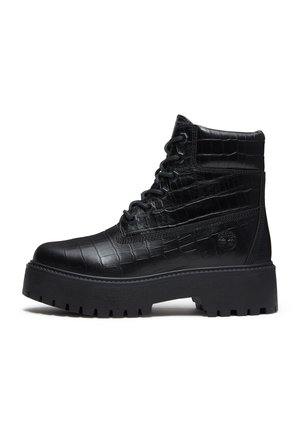 Botte noire montante lacée avec semelle épaisse à crampons et motif effet crocodile, conçue pour un usage robuste ou décontracté.