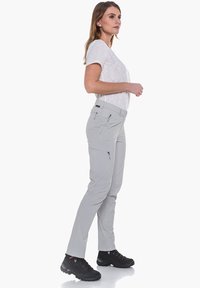 Pantalones de senderismo en gris claro con bolsillos con cremalleras, hechos de material duradero, combinados con zapatos de senderismo negros con cordones, sobre un modelo de perfil.