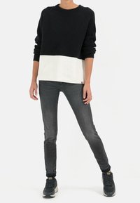 Sudadera de punto acanalado en blanco y negro con un ajuste relajado, combinada con jeans oscuros ajustados y zapatillas grises.