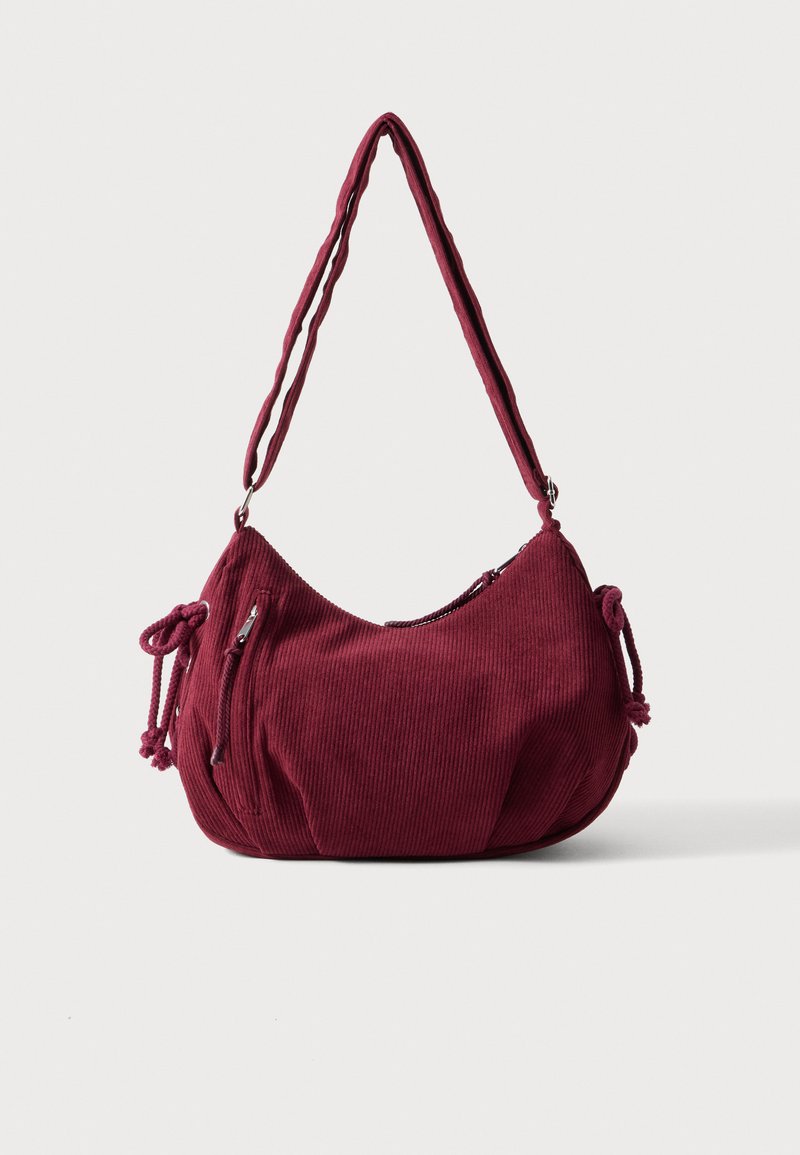 Sac d'épaule en velours côtelé bordeaux doux avec une sangle réglable, fermeture éclair, liens latéraux et une poche avant zippée.