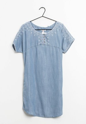 Vestido azul claro de manga corta con bordado geométrico blanco en las mangas y el escote, colgado en una percha negra sobre fondo blanco.