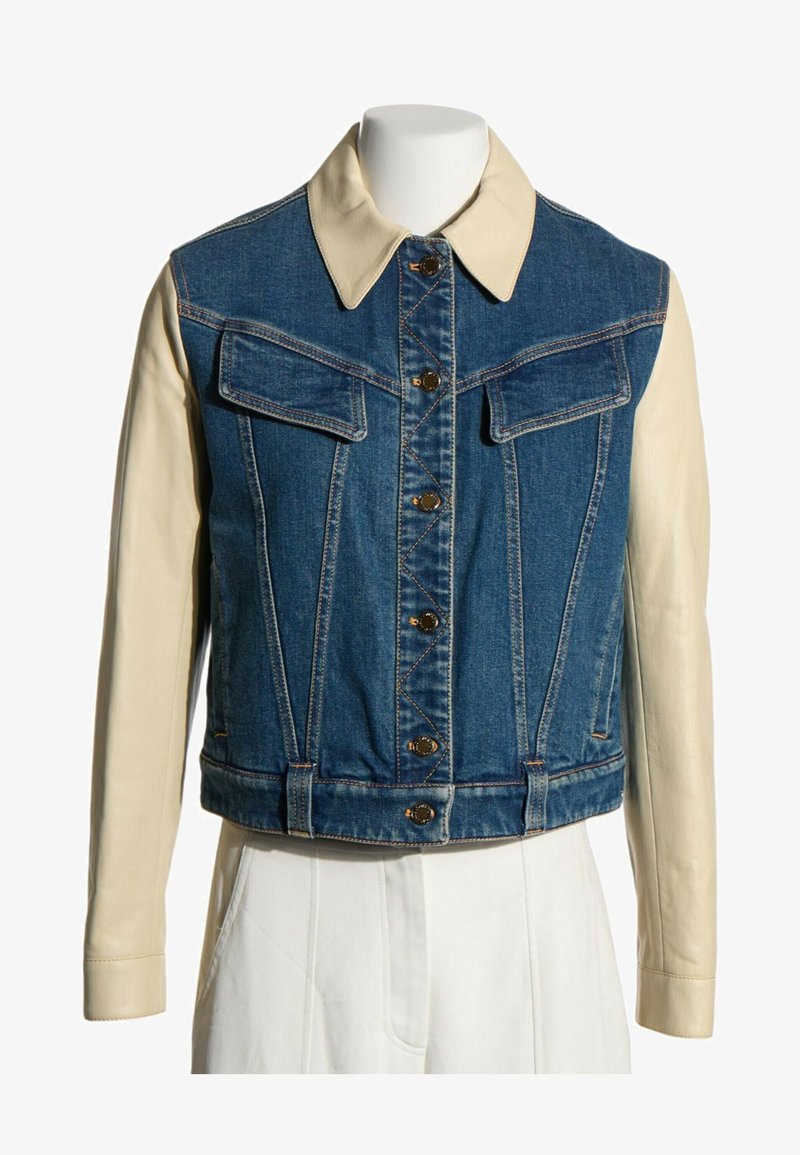 Veste en jean avec manches et col en cuir beige, fermeture à boutons sur le devant et deux poches à rabat sur la poitrine sur un mannequin blanc.