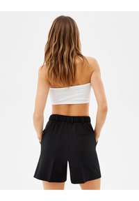 Černé kraťasy s elastickým pasem, mají zadní kapsu a sklady. Modelka má na sobě bílé ribované crop top.