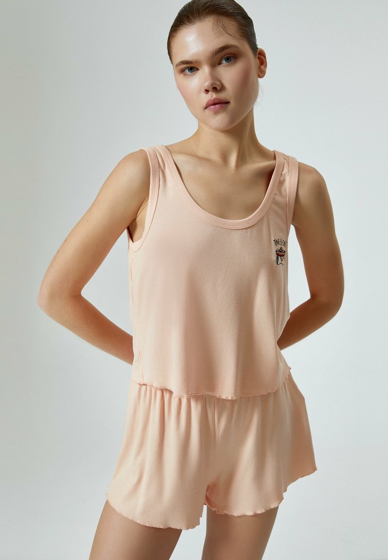 Peachfarvet to-delt sæt bestående af en ribbet tanktop med rund halsudskæring og shorts med elastisk talje. Stoffet ser blødt og let ud.