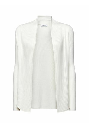 Femme portant un haut rouge, un cardigan blanc côtelé et une jupe plissée grise avec un petit motif géométrique, tenant les bords du cardigan ouverts.