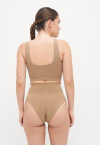 Bralette marrone senza cuciture e slip a vita alta. Materiale morbido e elastico con una texture liscia. Design minimalista, senza parti metalliche visibili.