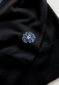 Black knit fabric with a textured appearance, featuring a light blue embroidered flower detail on one side.