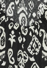 Sort-hvide mønstrede stof med paisley- og blomstermotiver, der har en samlet halsudskæring og en tekstureret overflade.