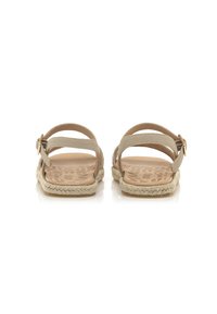 Sandalias con suelas planas, correas de cuero beige y un acento de yute al estilo espadrille. Cuentan con una hebilla en tono dorado y una plantilla texturizada.