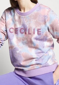 Felpa leggera con un motivo tie-dye rosa e blu, caratterizzata dal nome "CECILIE" in lettere testurizzate viola e un collo lilla.