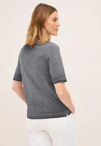 Haut gris à manches courtes avec une texture douce et des poignets roulés, associé à un jean blanc. L'arrière présente un léger détail à fente au niveau de l'ourlet.