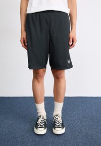 Svart netting sportshorts med elastisk midje, med en hvit logodetalj, kombinert med hvite crew-sokker og svarte joggesko.