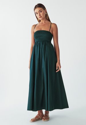 Dunkelgrünes, ärmelloses Maxikleid mit einem smockierten Oberteil und fließendem Rock. Es hat dünne Träger und besteht aus leichtem Stoff.