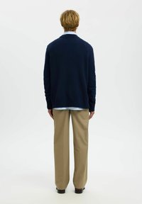 Pull en laine bleu marine avec un col châle, porté par-dessus une chemise à col bleu clair, associé à un pantalon beige. Texture lisse, coupe décontractée.