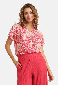 Short-sleeve, V-neck blouse with a pink and white wavy pattern, made of lightweight fabric, paired with textured pink high-waisted pants.