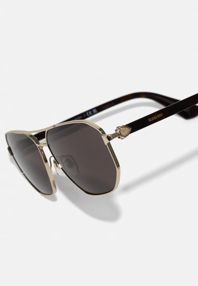 Óculos de sol octogonais com lentes escuras, armação em metal dourado e hastes em padrão tartaruga preto. Apresenta o logótipo da Burberry e detalhes decorativos.