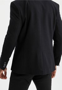 Czarna marynarka z teksturowanej tkaniny, o kroju dopasowanym, z bocznymi kieszeniami i mankietami na cztery guziki. Czyste linie i minimalistyczny design.