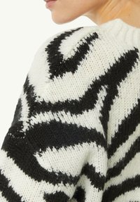Sweter dzianinowy z czarno-białym wzorem w zebry. Teksturowany materiał z okrągłym dekoltem i widocznymi ściegami dzianiny.