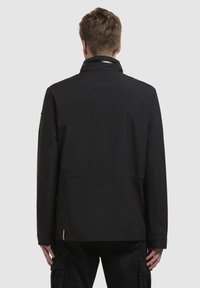 Svart jacka med rak skärning, med ståkrage och en slät, texturerad yta. Långa ärmar och minimalistisk design.