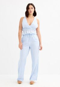 Mono azul claro de material suave, con escote en V profundo, cintura fruncida y pantalones de pierna ancha. Textura lisa y diseño informal.
