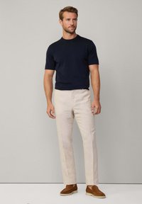 Marineblå kortærmet strikskjorte parret med lysebeige linnedbukser og brune ruskindsko, med et tætsiddende design og neutrale farver.