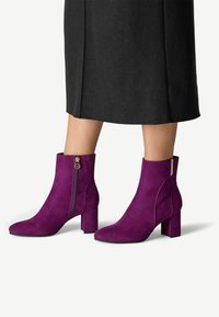 Fialové semišové kotníkové boty s kulatou špičkou, blokovým podpatkem a bočním zipem. Hladký povrch a elegantní design vhodný pro různé outfity.