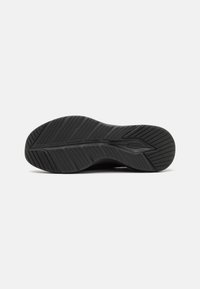 Black rubber shoe sole with a textured pattern, featuring grooves for traction and an embossed logo. Curved shape and flexible design.