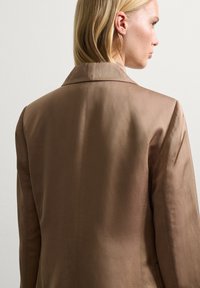 Bruine op maat gemaakte blazer met een gladde, satijnen uitstraling en een klassieke revers. Heeft minimale stikseldetails en gestructureerde schouders.