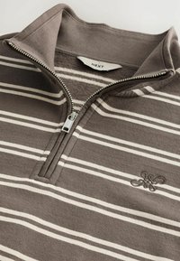 Brunstribet pullover med en lynlås krave. Har hvide striber og broderet logo. Fremstillet af blødt stof. Lynlås hardware er sølv.