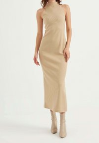 Beige ribbed maxi dress with a high neckline and fitted silhouette, paired with light beige slouchy ankle boots.