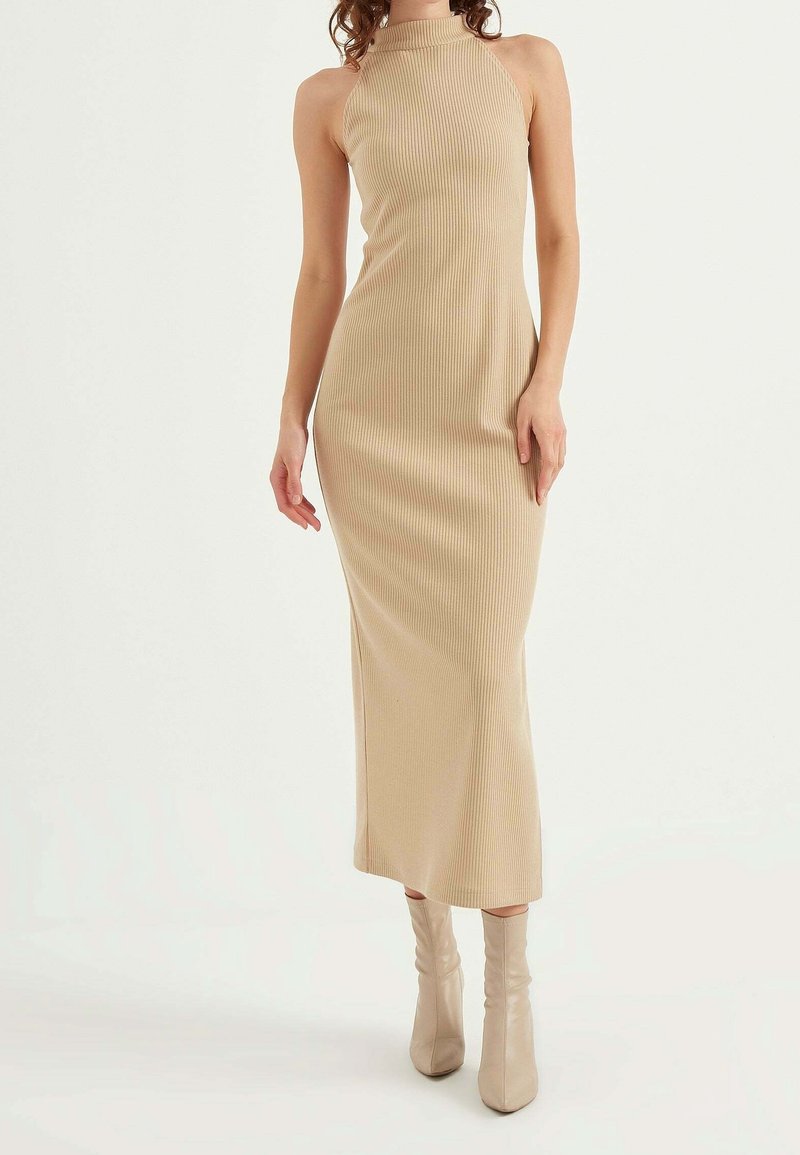 Beige ribbed maxi dress with a high neckline and fitted silhouette, paired with light beige slouchy ankle boots.