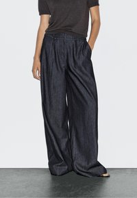 Wijde, donkere spijkerbroek met een gladde textuur en een elastische tailleband, gecombineerd met een aansluitend donker topje. Minimalistisch ontwerp zonder zichtbare patronen.