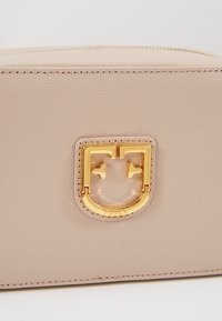 Porte-monnaie en cuir beige texturé avec fermoir en métal doré en forme de visage stylisé et coutures détaillées le long des bords.