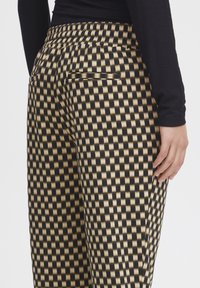 Pantalones a cuadros en negro y dorado con cinturilla elástica, que presentan una textura suave y bolsillos laterales, mostrados desde una perspectiva lateral.