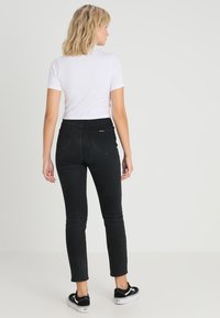 Jeans skinny noirs à taille haute, avec deux poches arrière et une finition lisse. Portés avec un t-shirt blanc et des baskets noires.