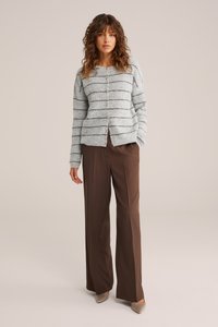 Šviesiai pilkas juostuotas megztinis su mygtukų uždarymu, pasižymintis minkšta tekstūra. Sutapatintas su rudais plačiakelniais kelnių ir smėlio spalvos šlifinimo bateliais.