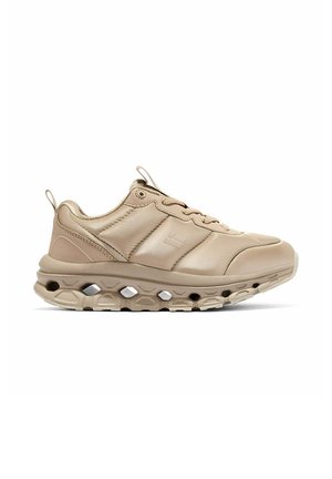 Zapatilla beige de perfil bajo con suela texturizada que presenta recortes hexagonales y cordones, mostrada en perfil lateral sobre un fondo blanco.