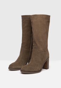 Bottes montantes en daim brun avec un bout arrondi et un talon en bois empilé, dotées d'une fermeture éclair latérale et d'une texture lisse.