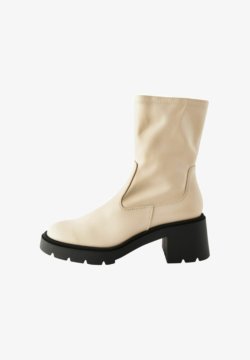 Beige enkellaars met een gladde leren afwerking, ronde neus, zij uitsparing en een stevige zwarte hak met een gestructureerde zool.