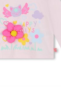 Chemise à manches longues rose clair avec un motif ludique représentant un chat, des cœurs, des nuages et des fleurs colorées, agrémentée d'une fleur rose 3D.
